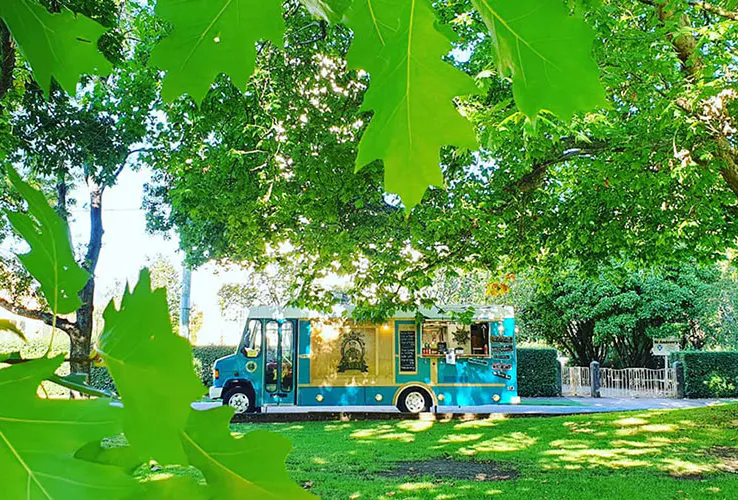 The teal and timber Sailor food truck parked beneath leafy trees in Tasmania